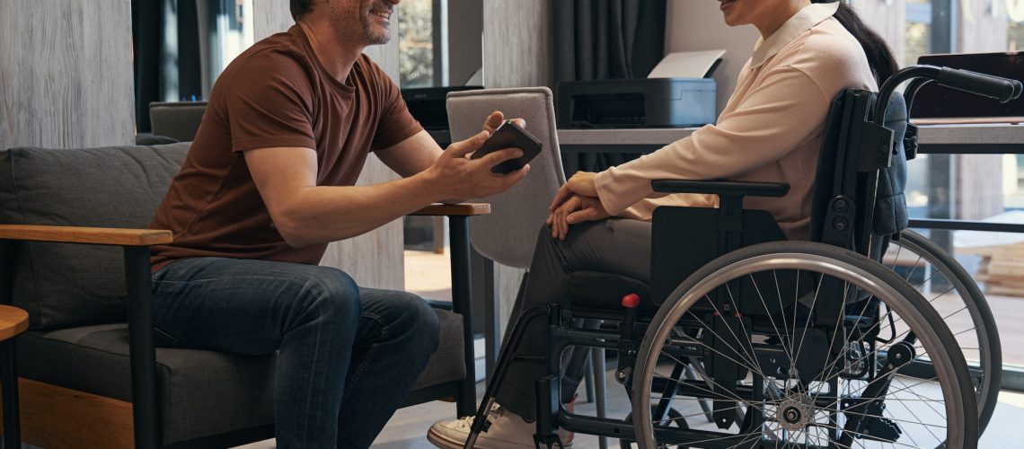 Jolly man with smartphone in office with female with disability